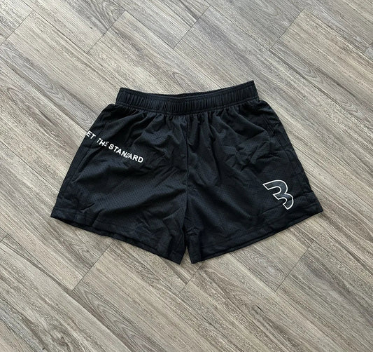 mesh shorts de la merch de CBUM en color negro, con una B de su logo en blanco y negro y la frase "set the standard" en blanco